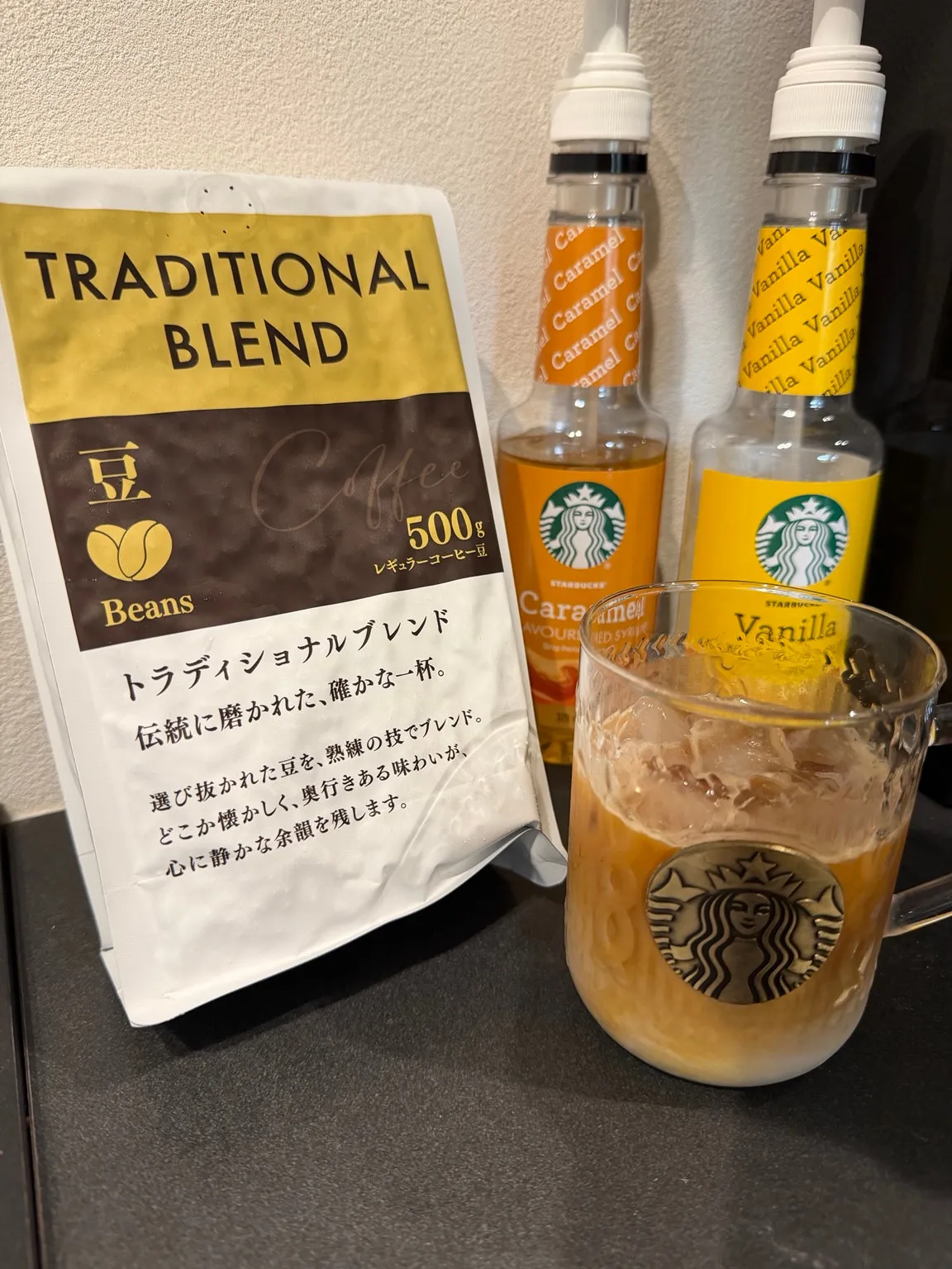 トラディショナルブレンドの500g袋、飲み物の入ったガラスカップ、キャラメルとバニラのシロップボトル